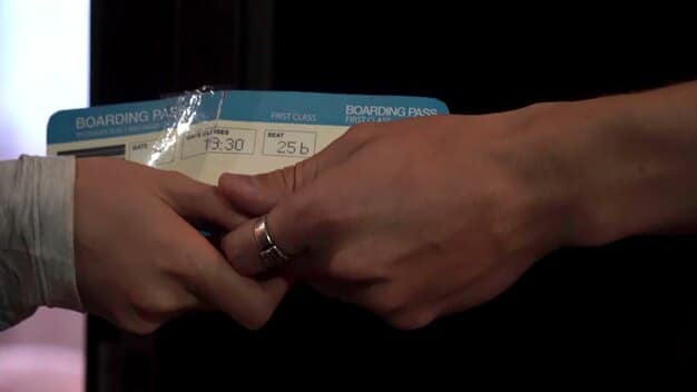 A close-up shot of an airline ticket showing a departure gate and time, with a blurred image of passengers boarding in the background, highlighting the increase in travel confirmations and passenger flow.