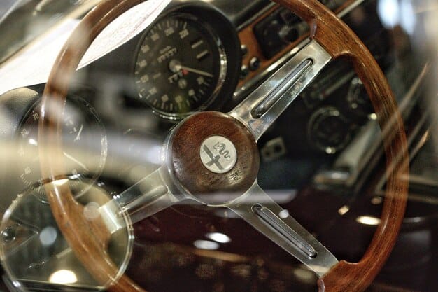 A close-up shot of a vintage car's dashboard, featuring analog gauges, a wooden steering wheel, and chrome accents. The focus is on the details and the craftsmanship of the interior.