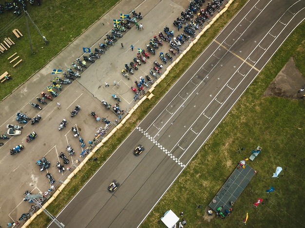 A high-angle shot of a diverse group of cars lined up at a race track, ready for a motorsport event. Drivers are seen in the foreground, preparing their vehicles, highlighting the competitive spirit and technical preparation involved in motorsports clubs.