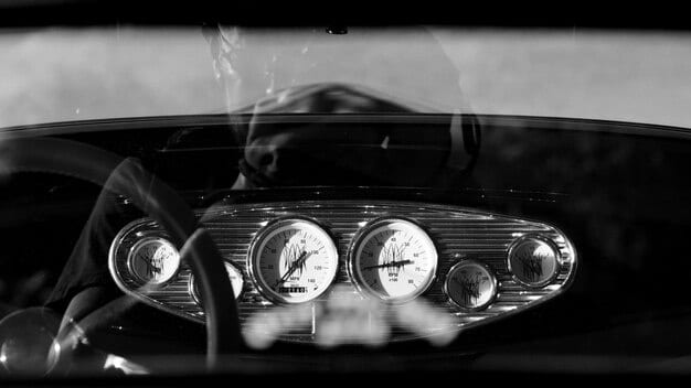 A close-up shot of a vintage car's dashboard during a classic car rally, focusing on the intricate gauges and steering wheel. The driver's hands are visible, showcasing the engagement required to navigate the vehicle.