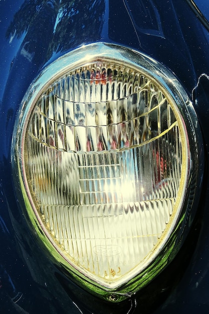 A close-up shot of a car's headlight, showcasing the intricate design and reflecting the surrounding environment. The image should have a shallow depth of field, blurring the background to emphasize the headlight's details, and use soft, diffused lighting to highlight the textures and contours.