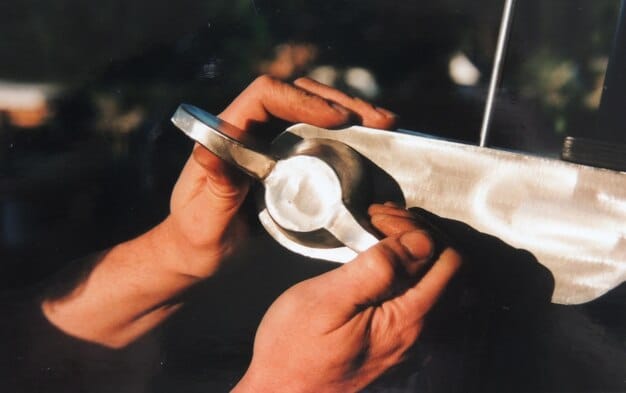 A close-up shot of a restorer's hands carefully polishing a chrome bumper of a vintage car. The restorer is wearing gloves and using specialized polishing tools to bring out the shine and luster of the chrome, demonstrating the care and precision involved in the restoration process.