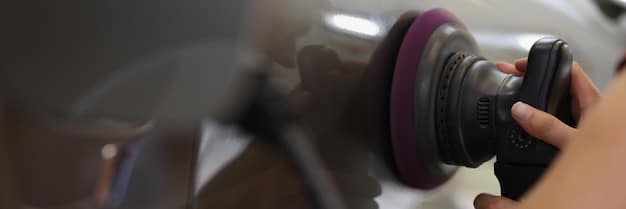A professional car detailer carefully polishing a car's paint surface with a machine polisher in a well-lit garage.