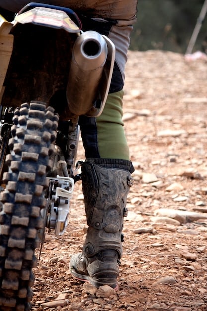 A close-up shot of an adventure touring motorcycle's suspension system, highlighting its adjustability and robust design. The suspension is shown navigating a rocky off-road trail.